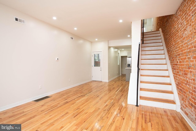 unfurnished living room with light hardwood / wood-style flooring and brick wall