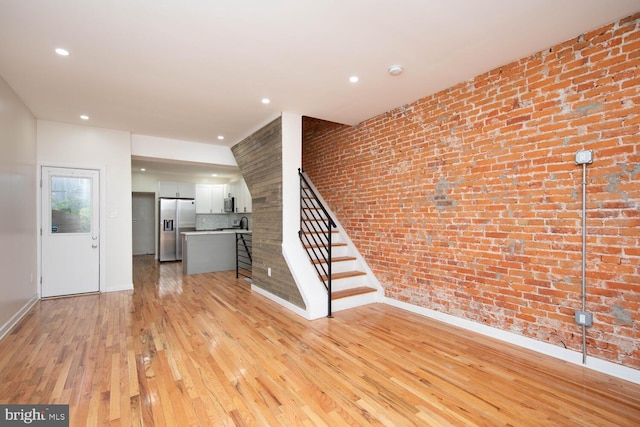 unfurnished living room with light wood-type flooring and brick wall