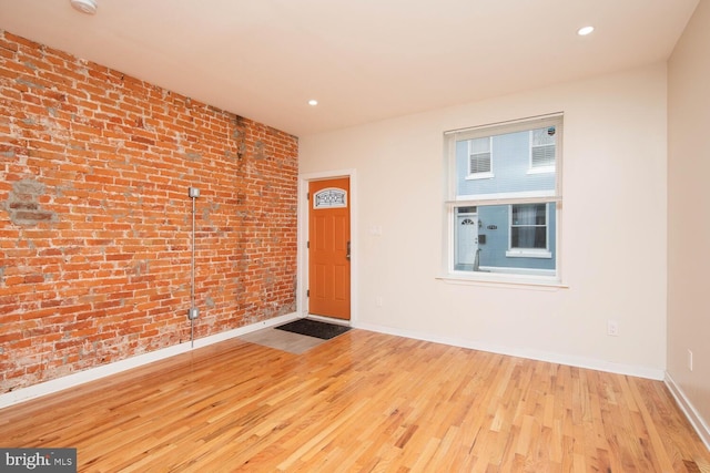 unfurnished room featuring light hardwood / wood-style floors and brick wall