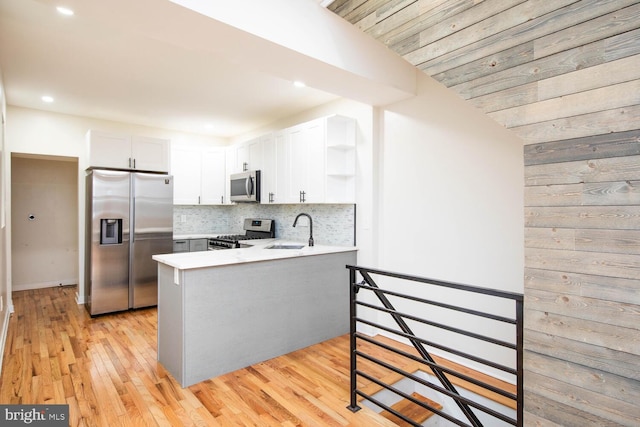 kitchen featuring white cabinetry, sink, light hardwood / wood-style flooring, kitchen peninsula, and appliances with stainless steel finishes