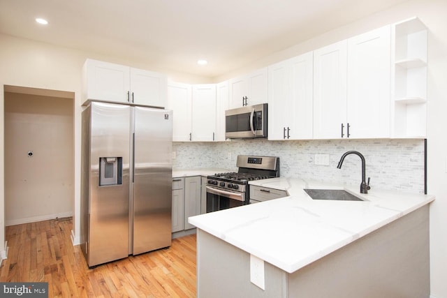 kitchen with kitchen peninsula, sink, light stone countertops, appliances with stainless steel finishes, and white cabinetry