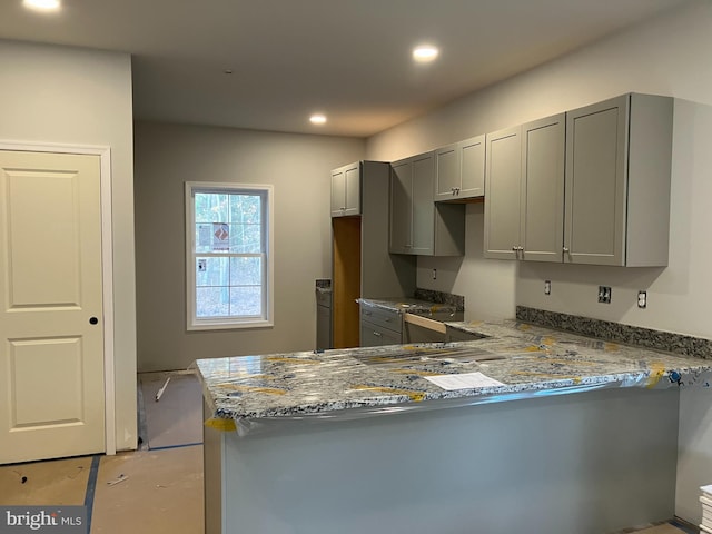 kitchen with kitchen peninsula, stone counters, and gray cabinetry