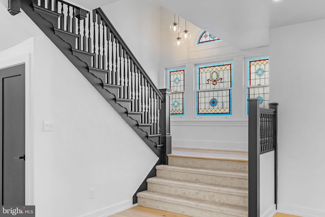 staircase with hardwood / wood-style floors, a towering ceiling, and an inviting chandelier