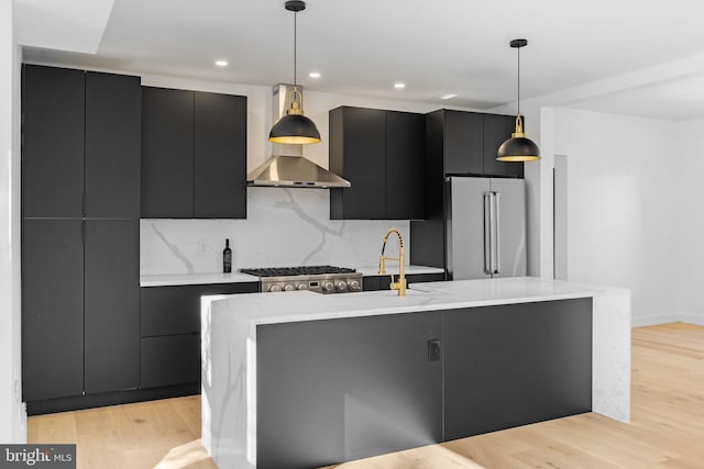 kitchen with appliances with stainless steel finishes, light hardwood / wood-style floors, hanging light fixtures, and a kitchen island with sink