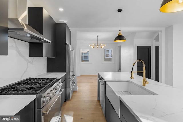 kitchen with wall chimney range hood, decorative light fixtures, light wood-type flooring, premium appliances, and a chandelier