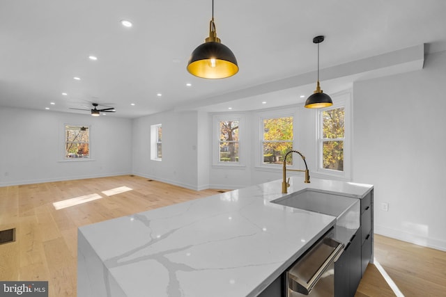 kitchen with light stone countertops, stainless steel dishwasher, a kitchen island with sink, decorative light fixtures, and light hardwood / wood-style flooring