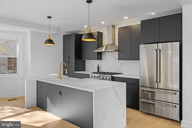 kitchen featuring a kitchen island with sink, decorative light fixtures, stainless steel appliances, and wall chimney range hood