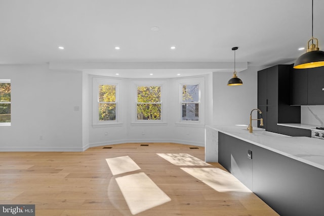 kitchen with light stone counters, light hardwood / wood-style flooring, and pendant lighting