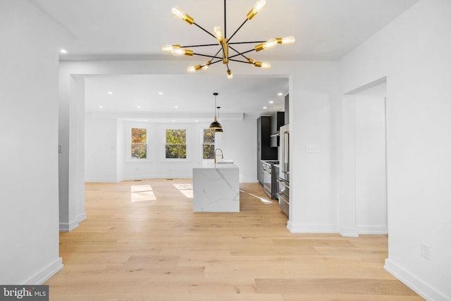 kitchen featuring sink, hanging light fixtures, an island with sink, light hardwood / wood-style floors, and light stone counters