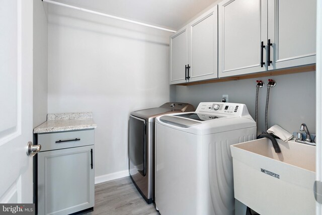 washroom featuring cabinets, washing machine and dryer, light hardwood / wood-style floors, and sink