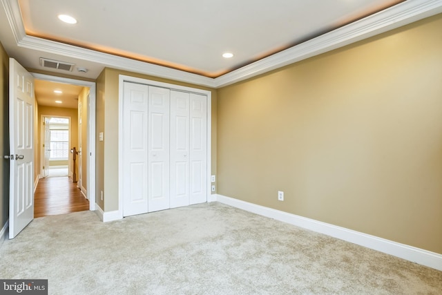 unfurnished bedroom featuring a tray ceiling, light carpet, a closet, and ornamental molding