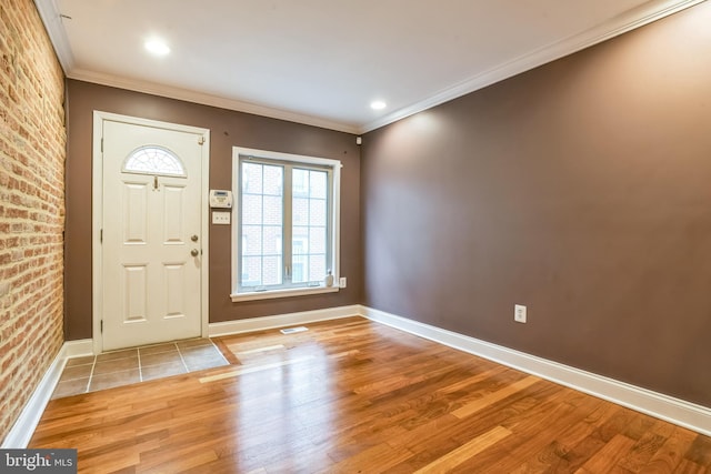 foyer entrance featuring light hardwood / wood-style floors, ornamental molding, and brick wall