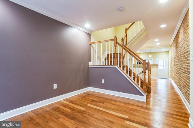 staircase with crown molding, wood-type flooring, and brick wall