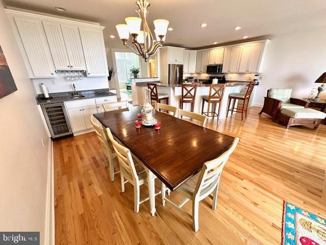 dining space with a notable chandelier, light hardwood / wood-style floors, and beverage cooler