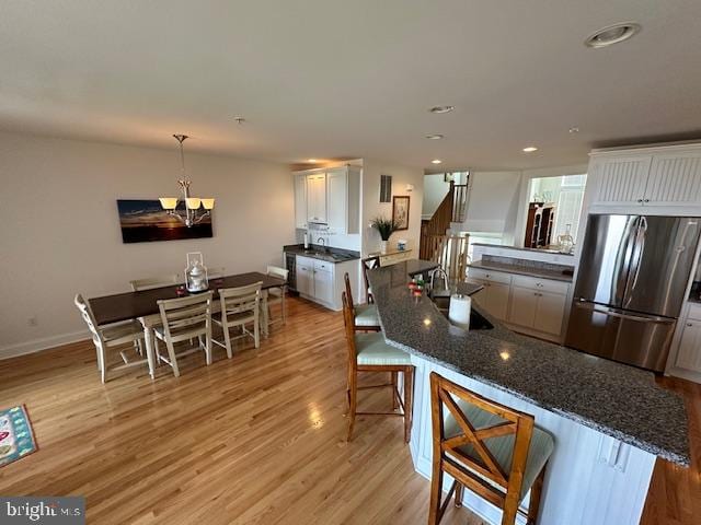 kitchen with a kitchen breakfast bar, light hardwood / wood-style floors, white cabinetry, and stainless steel refrigerator