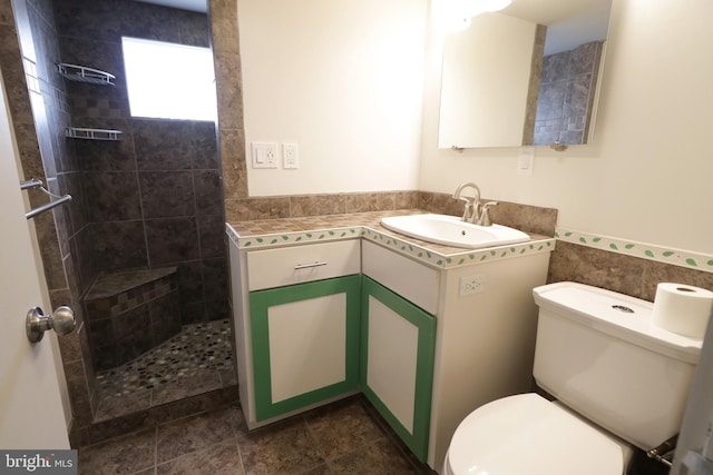 bathroom with tiled shower, vanity, tile walls, and toilet