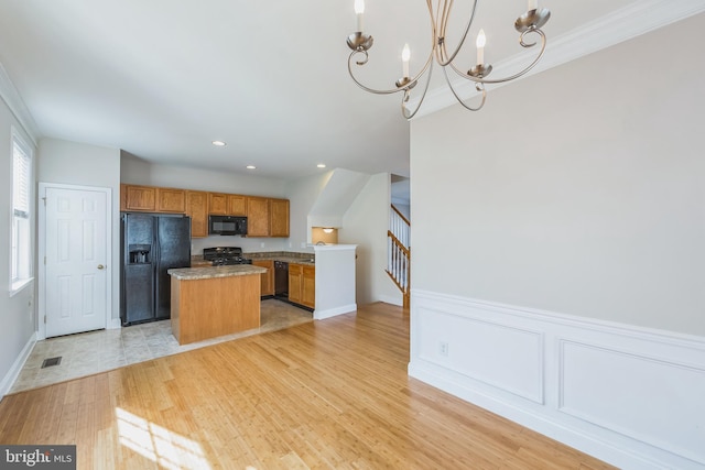 kitchen with black appliances, pendant lighting, an inviting chandelier, light hardwood / wood-style flooring, and a center island