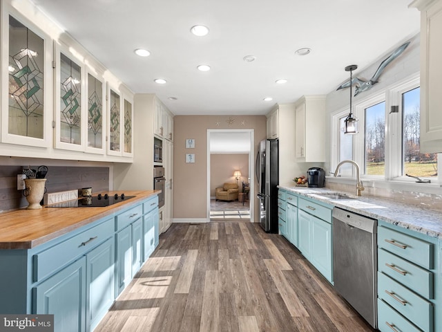 kitchen with sink, appliances with stainless steel finishes, decorative light fixtures, white cabinetry, and wood-type flooring