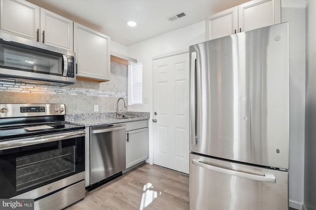 kitchen featuring light stone countertops, light wood-type flooring, stainless steel appliances, and white cabinetry