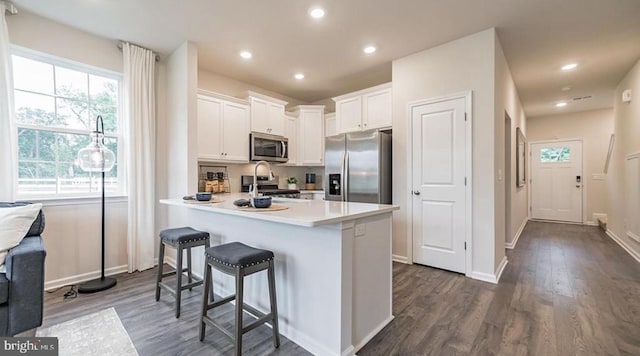 kitchen with a kitchen bar, kitchen peninsula, stainless steel appliances, dark wood-type flooring, and white cabinets