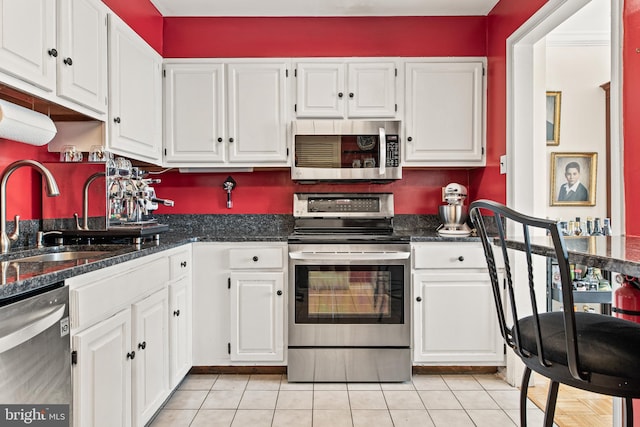 kitchen featuring white cabinetry, sink, stainless steel appliances, dark stone countertops, and light tile patterned floors