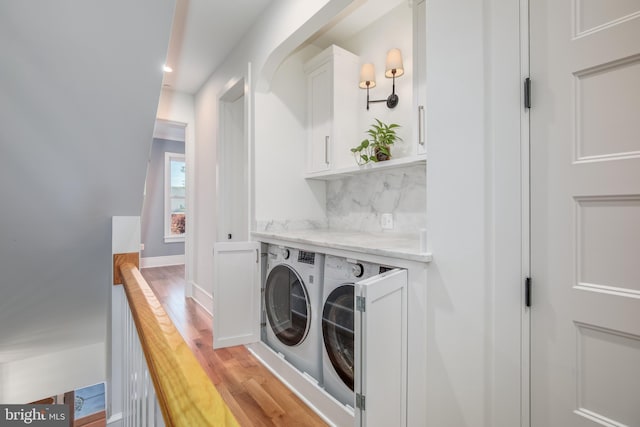 laundry area featuring washing machine and clothes dryer, light hardwood / wood-style flooring, and cabinets