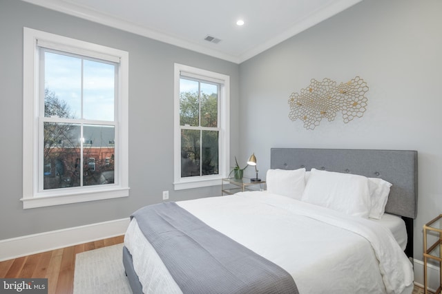 bedroom with hardwood / wood-style flooring, multiple windows, and crown molding