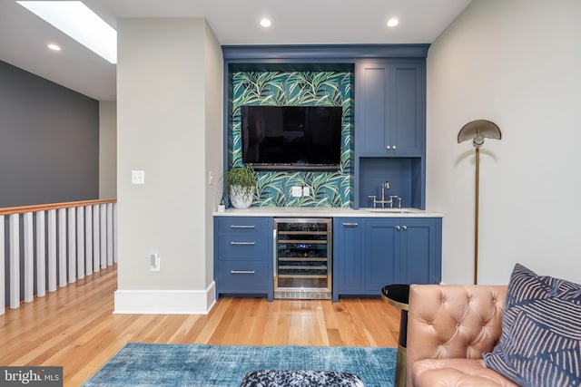 bar featuring blue cabinetry, sink, beverage cooler, and light wood-type flooring