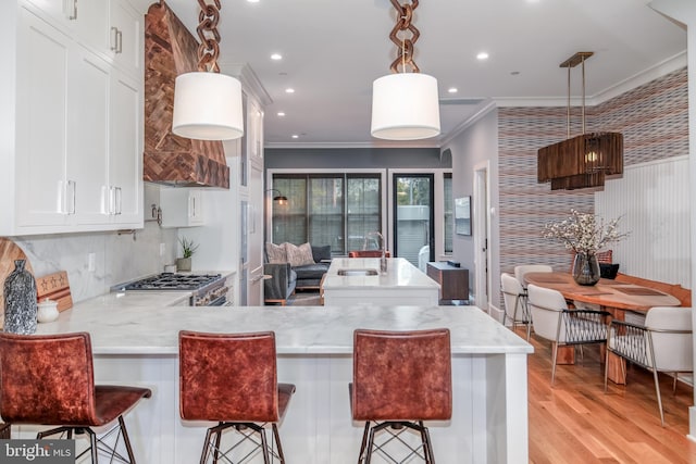 kitchen with a kitchen bar, crown molding, white cabinets, and hanging light fixtures