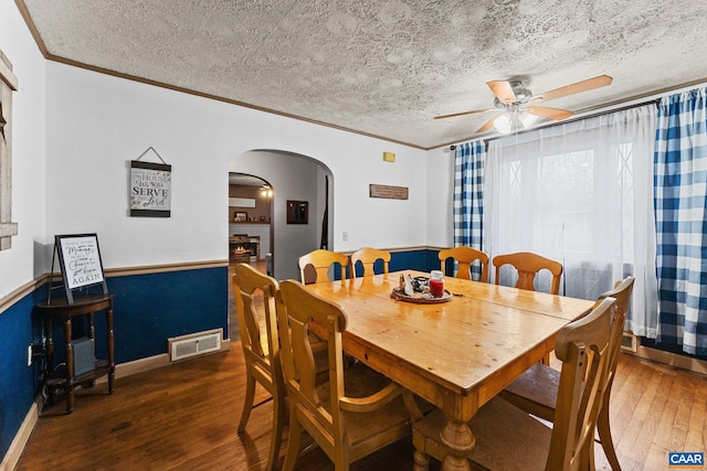 dining room with ceiling fan, dark hardwood / wood-style flooring, a textured ceiling, a fireplace, and ornamental molding