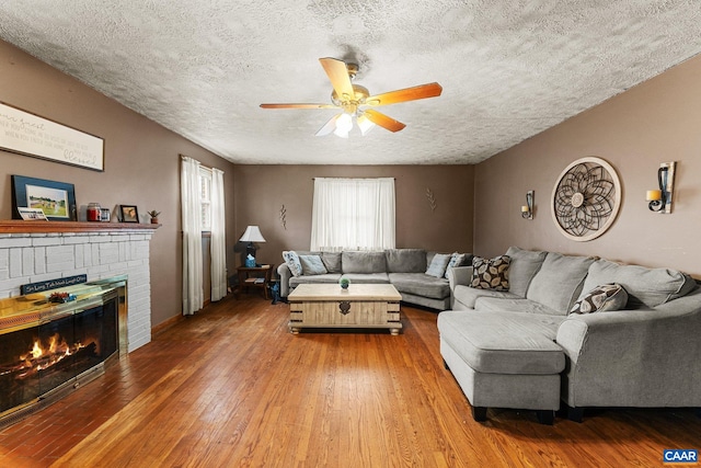 living room with hardwood / wood-style floors, a textured ceiling, a brick fireplace, and ceiling fan