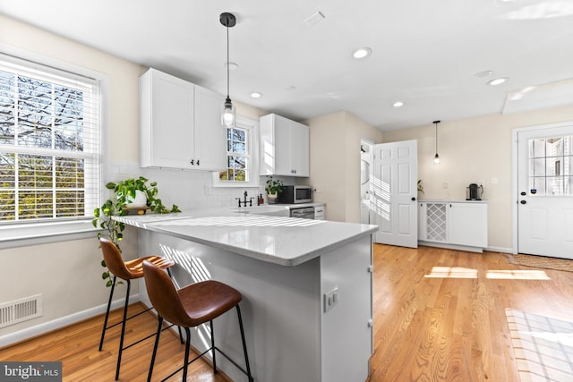 kitchen with kitchen peninsula, white cabinetry, a breakfast bar, and a healthy amount of sunlight