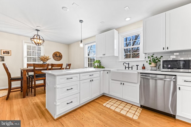 kitchen with sink, stainless steel appliances, light hardwood / wood-style floors, decorative light fixtures, and white cabinets