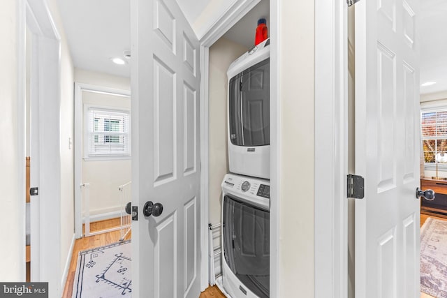 clothes washing area with hardwood / wood-style flooring and stacked washer / drying machine