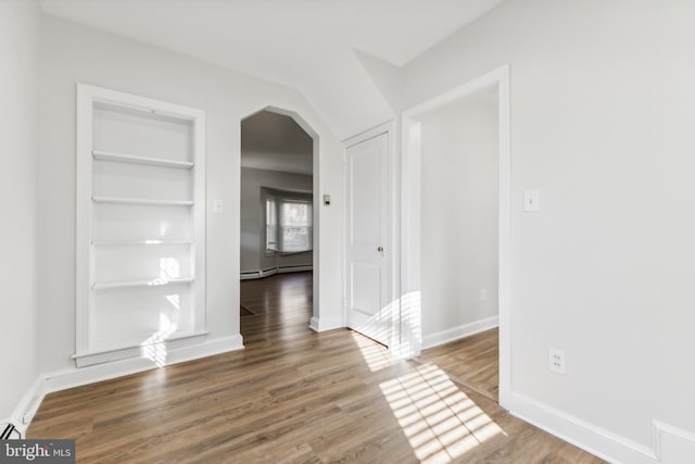 empty room featuring baseboard heating, built in features, and wood-type flooring