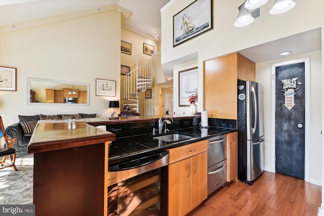 kitchen featuring a high ceiling, sink, light hardwood / wood-style flooring, stainless steel appliances, and beverage cooler