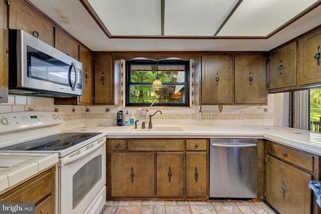 kitchen featuring tile counters, a healthy amount of sunlight, sink, and appliances with stainless steel finishes