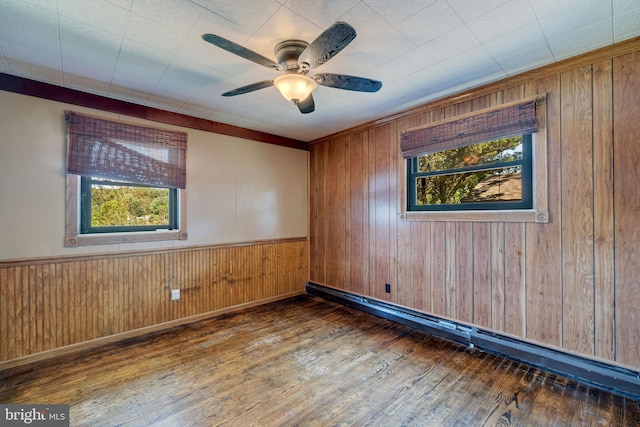 unfurnished room with a baseboard heating unit, ceiling fan, dark wood-type flooring, and wood walls