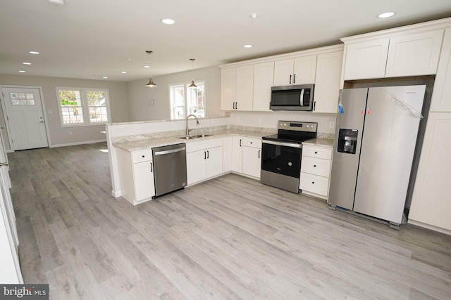 kitchen featuring appliances with stainless steel finishes, sink, light hardwood / wood-style flooring, white cabinets, and hanging light fixtures