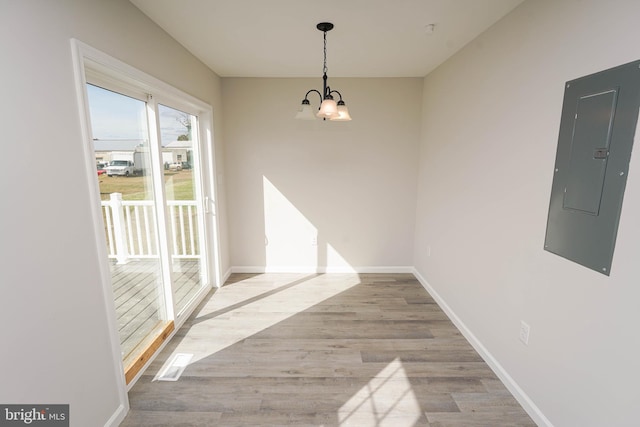 unfurnished dining area featuring electric panel, a chandelier, and light hardwood / wood-style floors