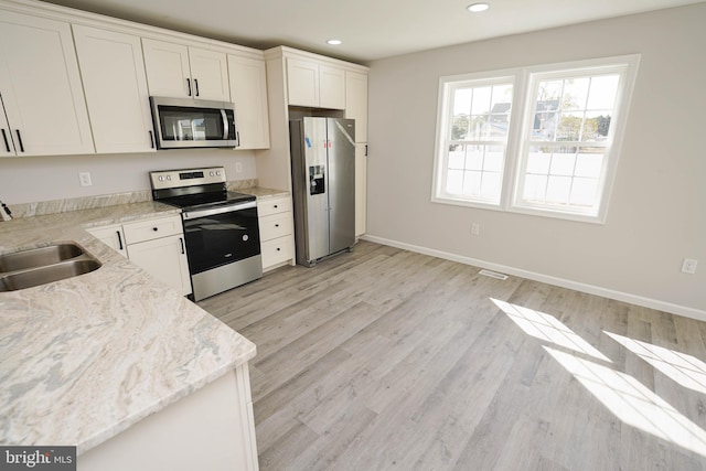 kitchen featuring light stone counters, stainless steel appliances, sink, light hardwood / wood-style flooring, and white cabinets