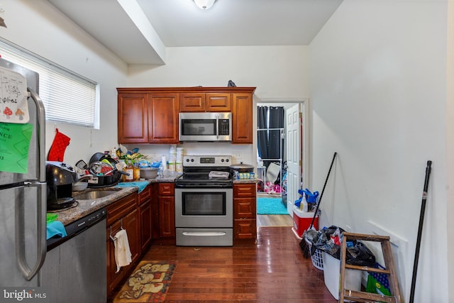 kitchen with sink, dark hardwood / wood-style flooring, dark stone counters, and appliances with stainless steel finishes