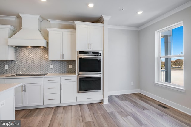 kitchen featuring white cabinets, crown molding, stainless steel double oven, light wood-type flooring, and custom range hood