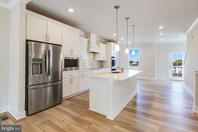 kitchen with light wood-type flooring, an island with sink, decorative light fixtures, white cabinetry, and stainless steel appliances