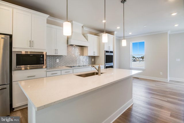 kitchen with white cabinets, premium range hood, stainless steel appliances, and a center island with sink