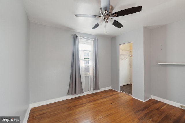 unfurnished bedroom featuring a walk in closet, a closet, hardwood / wood-style flooring, and ceiling fan