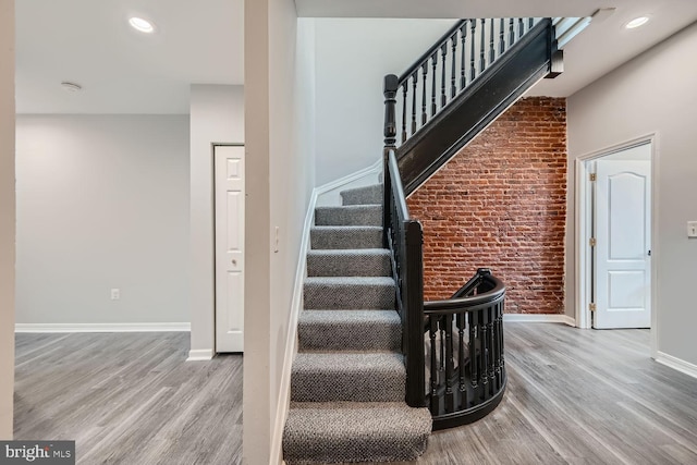 stairway with hardwood / wood-style floors and brick wall