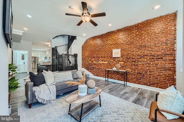 living room with ceiling fan, wood-type flooring, and brick wall