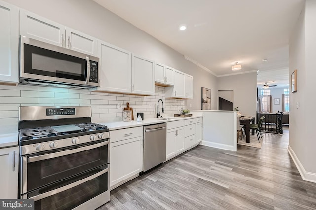 kitchen with ceiling fan, stainless steel appliances, light hardwood / wood-style flooring, white cabinets, and ornamental molding