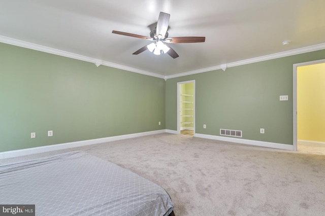 unfurnished bedroom with carpet flooring, a spacious closet, ceiling fan, and ornamental molding